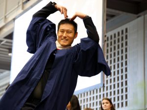 A graduate makes the shape of a heart with his hands while crossing the Convocation stage.