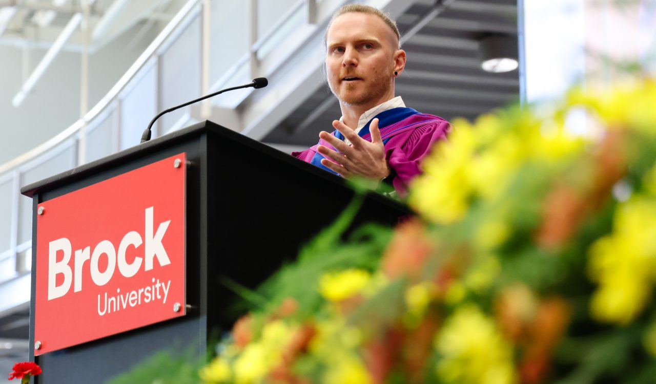 Associate Professor of Sport Management Kyle Rich wears a blue convocation gown and delivers a speech during the morning ceremony of Brock University's 116th Convocation.