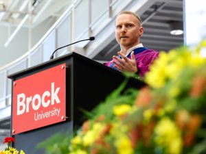 Associate Professor of Sport Management Kyle Rich wears a blue convocation gown and delivers a speech during the morning ceremony of Brock University's 116th Convocation.