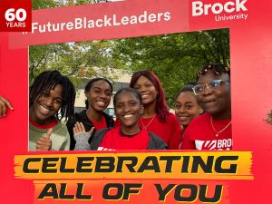 A group of high school and first-year university students pose for a photo outside holding a large red frame.