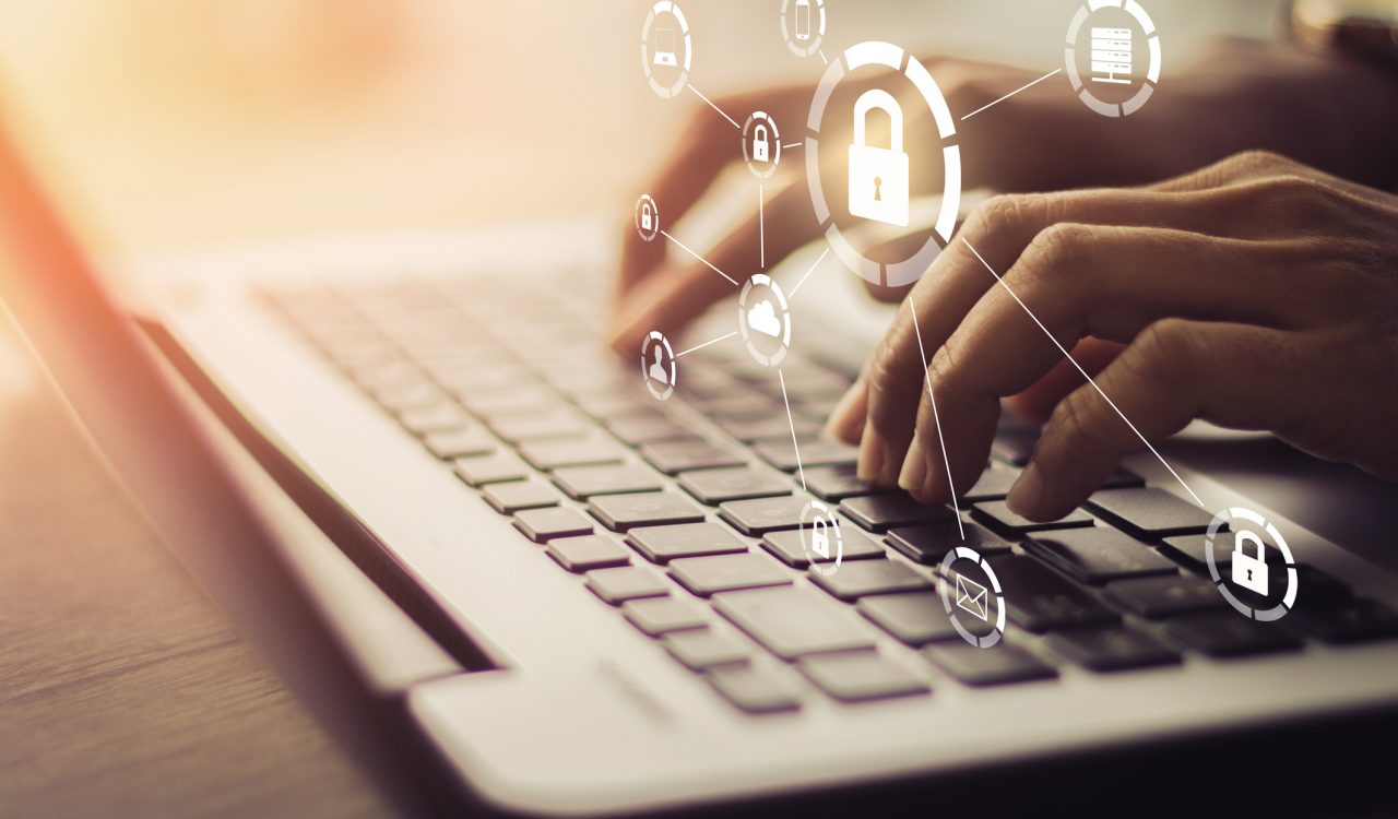 Close-up of hands typing on a laptop with cybersecurity icons floating above them.