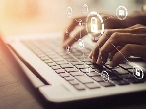 Close-up of hands typing on a laptop with cybersecurity icons floating above them.