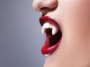 Close-up of mouth of a woman a woman wearing fake vampire teeth and red lipstick.