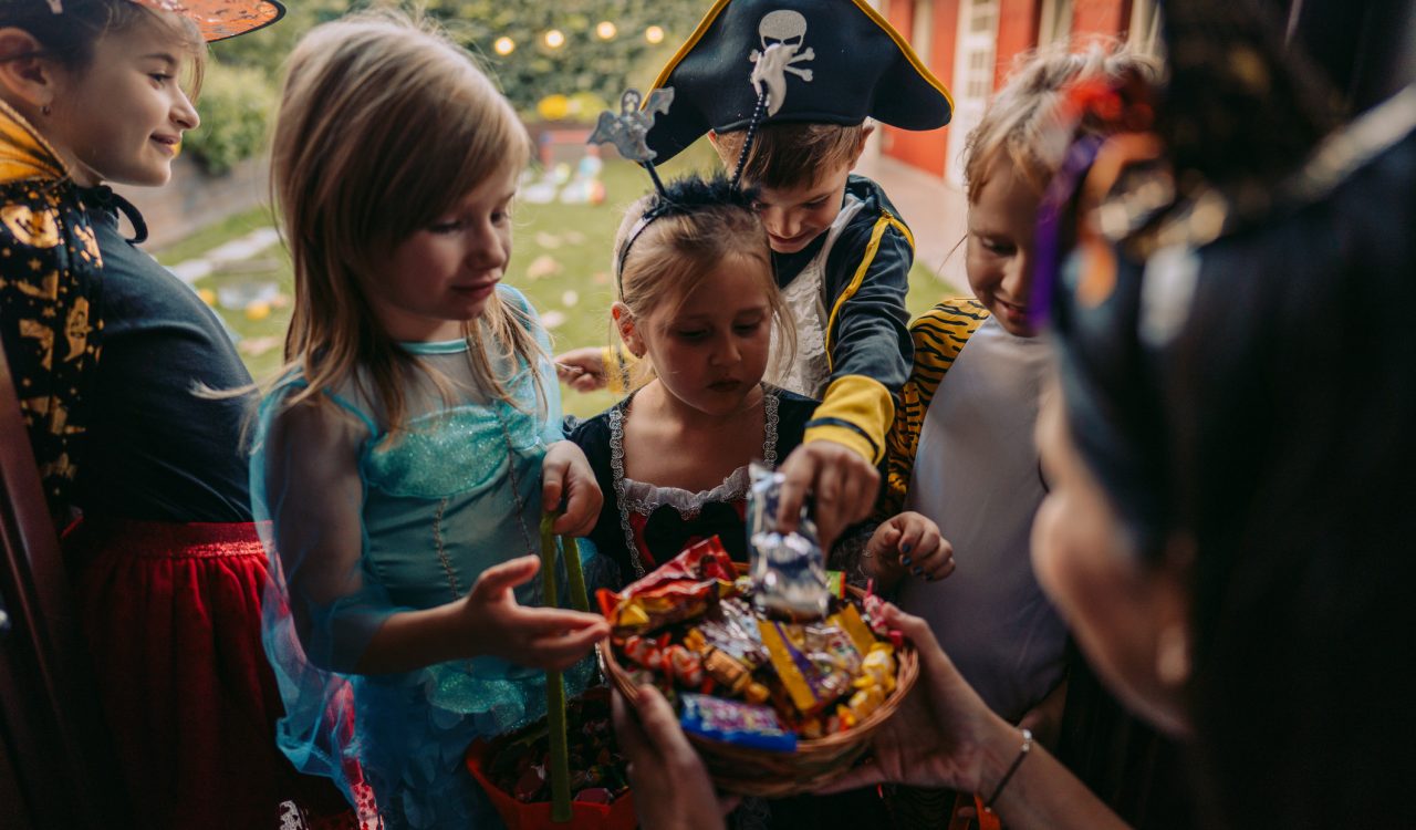 Children dressed in Halloween costumes gather on a doorstep to collect candy.