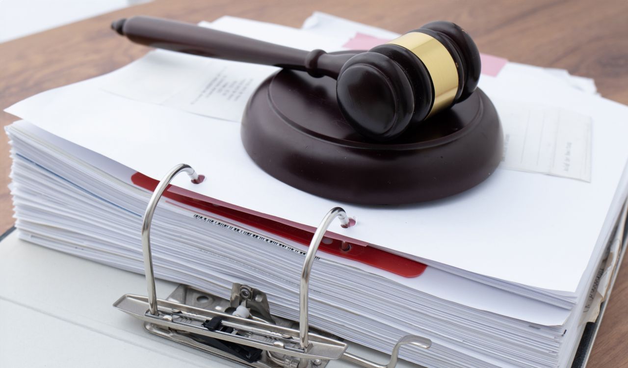 A gavel rests on top of a binder full of documents.