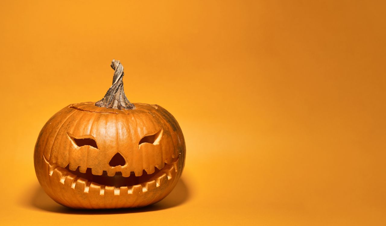 A pumpkin with a face carved into it sits on an orange backdrop.