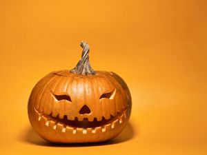 A pumpkin with a face carved into it sits on an orange backdrop.