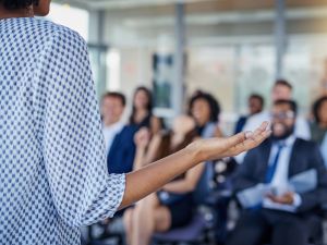 Close-up of the side of a business professional standing at the front of a room making a presentation to colleagues.