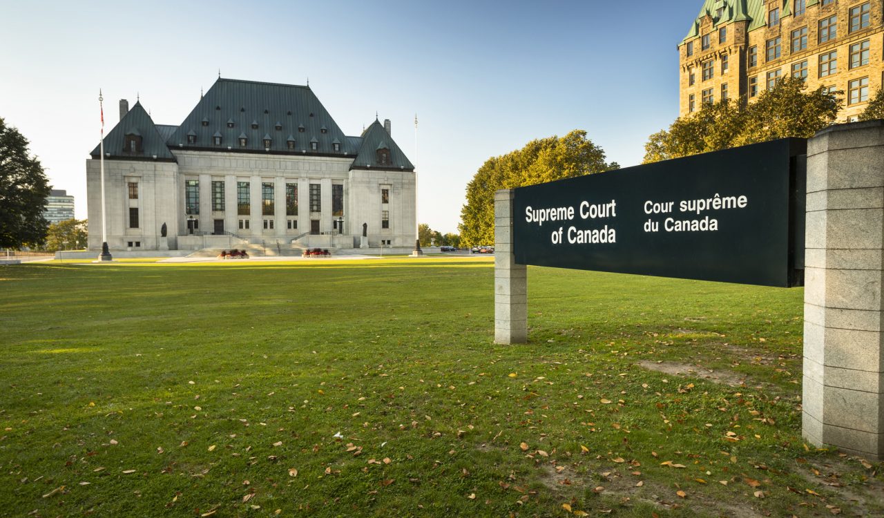 The Supreme Court of Canada in Ottawa, with a sign in the foreground on a bright green lawn.