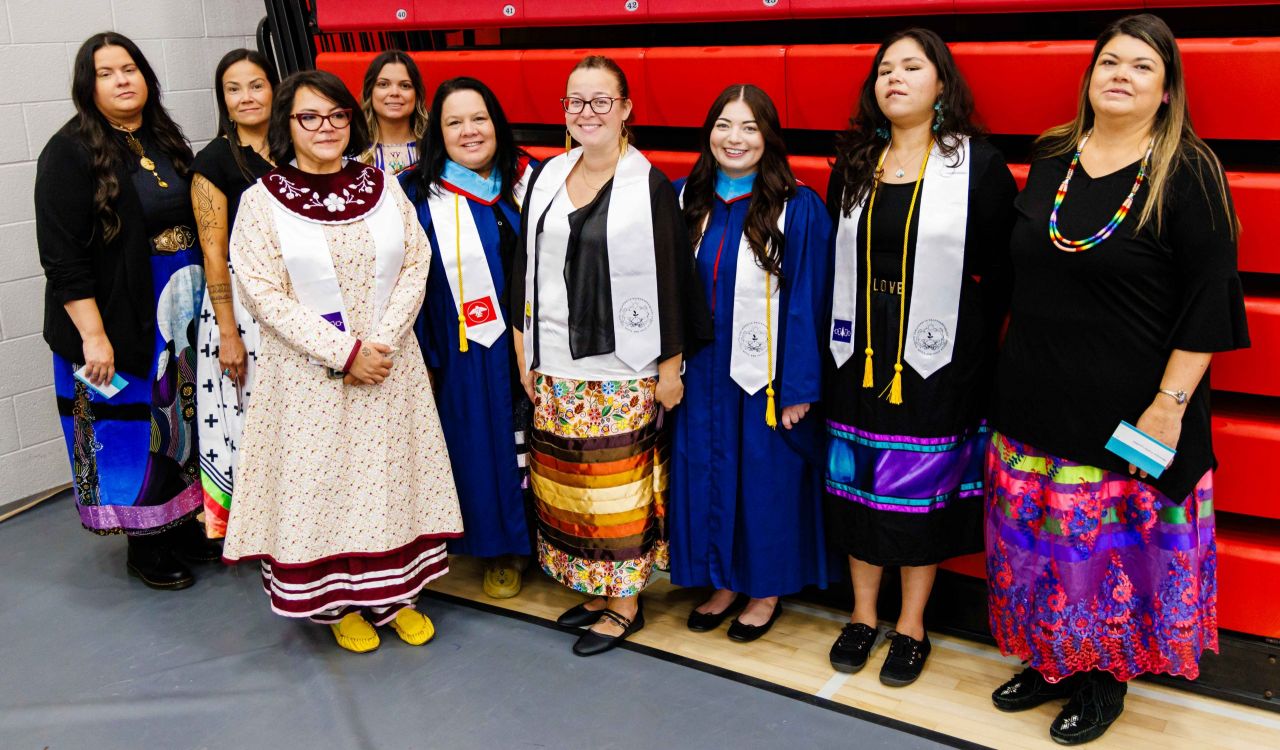 A group of Indigenous women stand shoulder to shoulder in a gymnasium smiling at the camera.