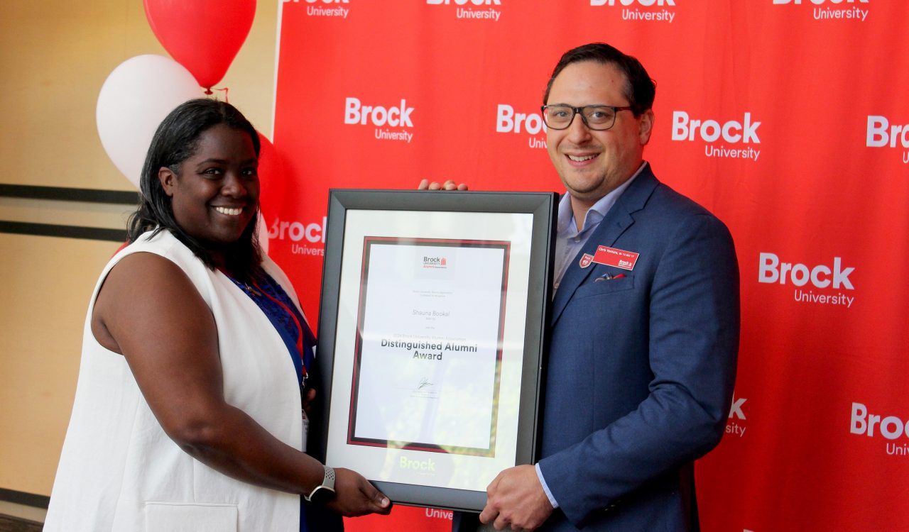 A man and a woman pose for a photo holding a framed certificate between them.