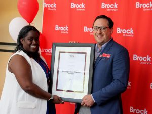 A man and a woman pose for a photo holding a framed certificate between them.