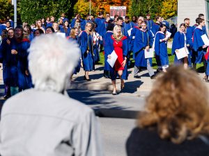 A group of graduates, led by one in a red dress, walks towards a group of seniors.