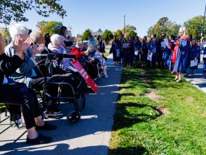 A graduate stands outside speaking with a group of seniors who are seated.