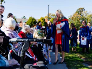 A graduate stands outside speaking with a group of seniors who are seated.