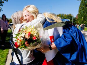 A woman in a graduation gown hugs an older woman.