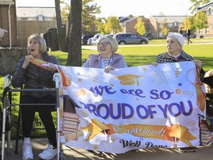 Three senior citizens hold a banner of congratulations.