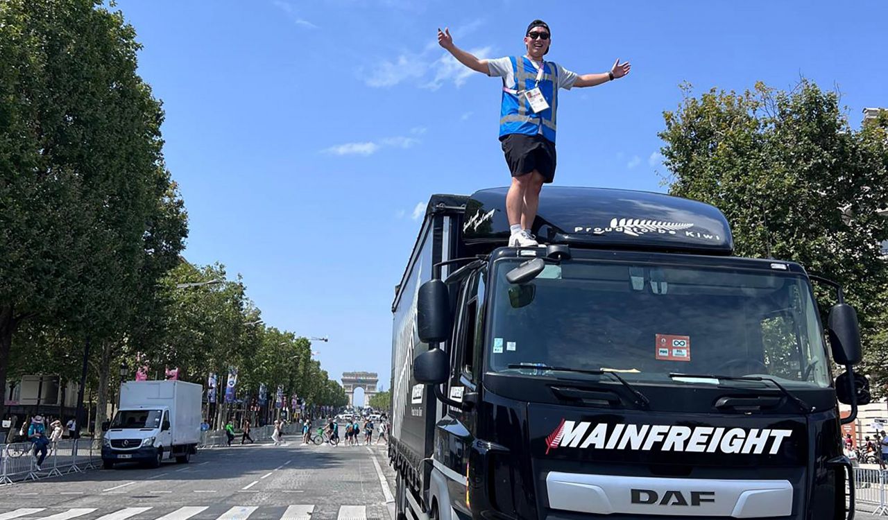 Man stands on black transport truck on the cobblestone roads of Paris France in front of the Arc de Triomphe.