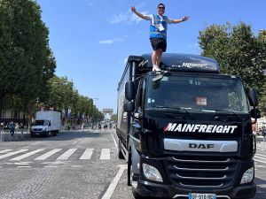 Man stands on black transport truck on the cobblestone roads of Paris France in front of the Arc de Triomphe.