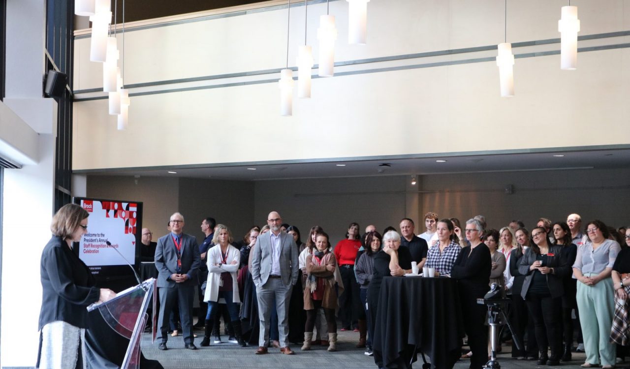 A group of people look on as a woman speaks at a podium during an awards ceremony.