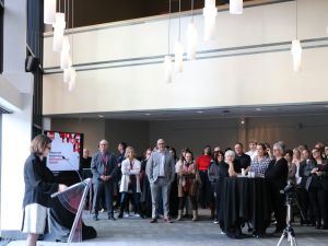 A group of people look on as a woman speaks at a podium during an awards ceremony.