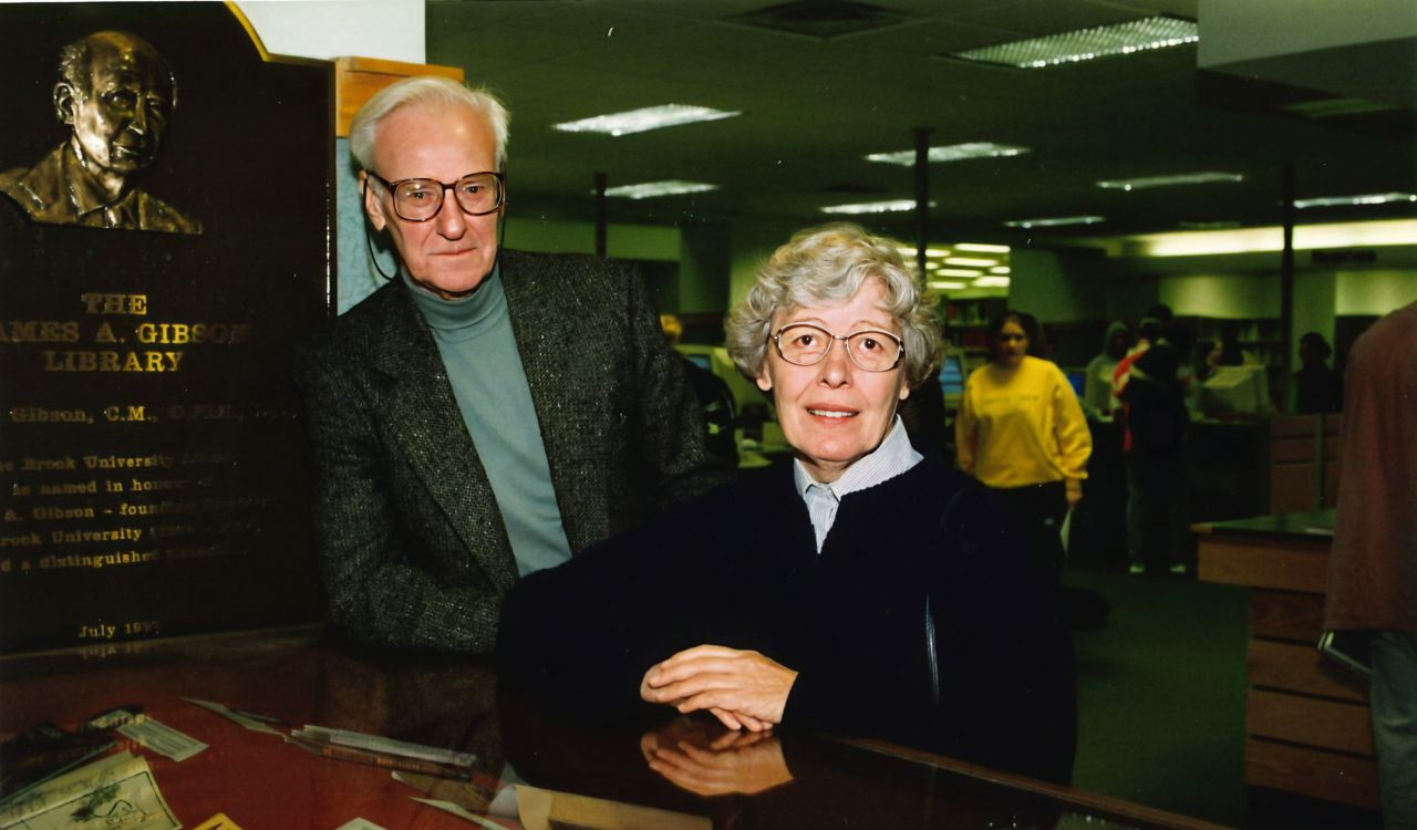 An older man and woman pose for a photo in a library.