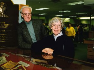 An older man and woman pose for a photo in a library.