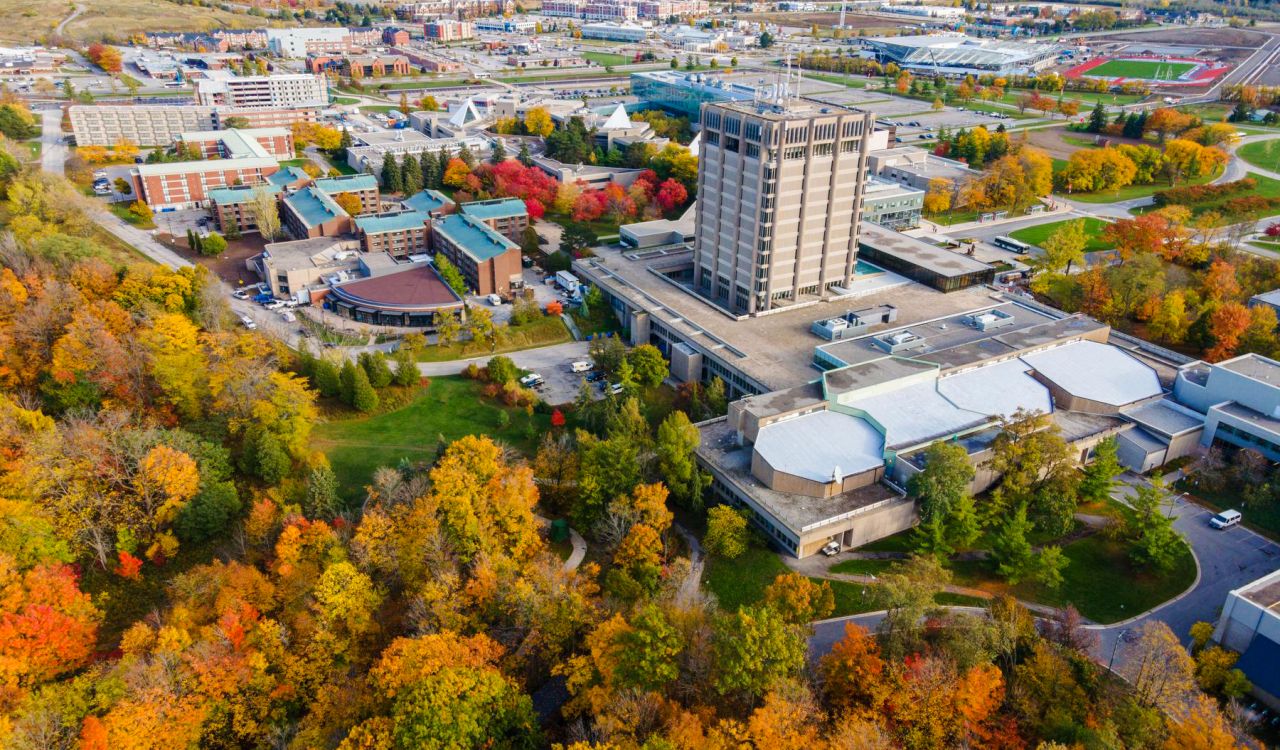 An aerial view of Brock University's main campus surrounded by trees with colourful fall leaves.