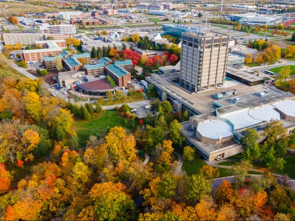 An aerial view of Brock University's main campus surrounded by trees with colourful fall leaves.
