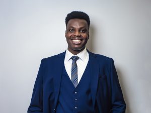 Tochukwu Daniel Oguejiofor stands against a neutral wall while wearing a blue formal suit.