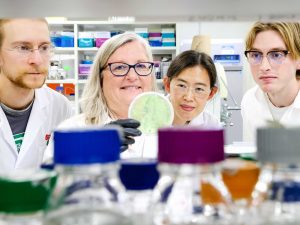 Four people in labcoats look at a petri dish being held up by one of the scientists.