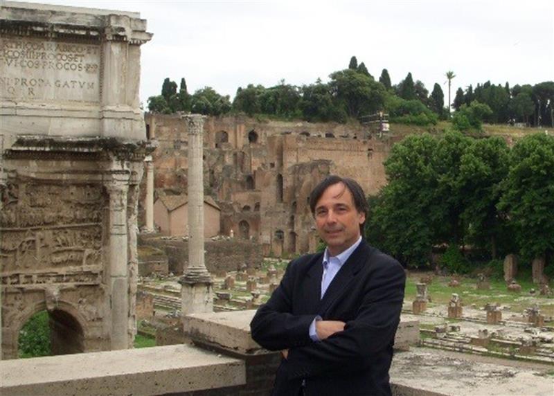 A man poses in front of historic ruins. 