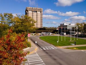 An aerial view of Brock University’s campus from the front with roadways, grass, trees and a blue sky with a tower building in the background.