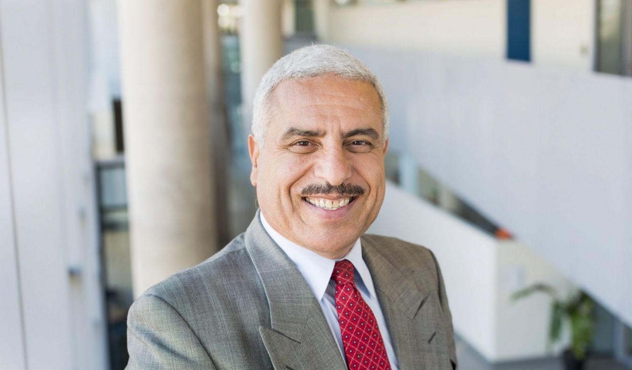 A man in a suit poses for a headshot in a sunny hallway.