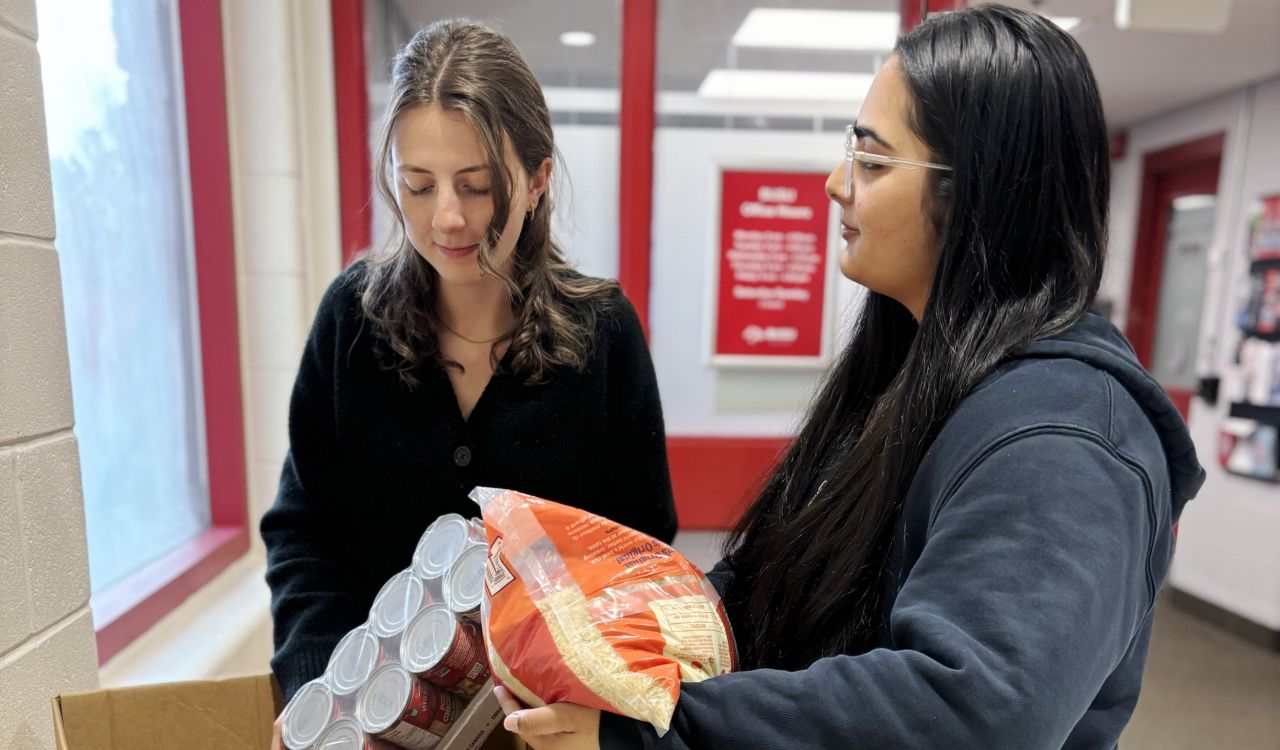 Two people place non-perishable food items into a donation bin.