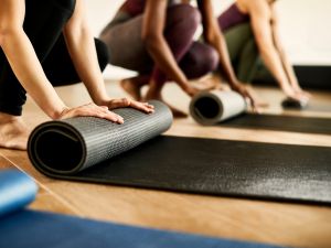 Close up of students in workout clothes kneeling down to roll up yoga mats.