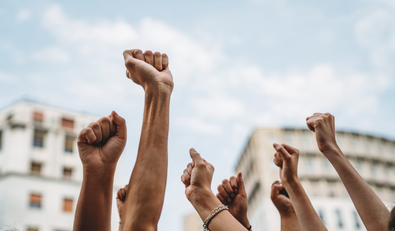 Fists of unseen striking demonstrators are raised against the sky