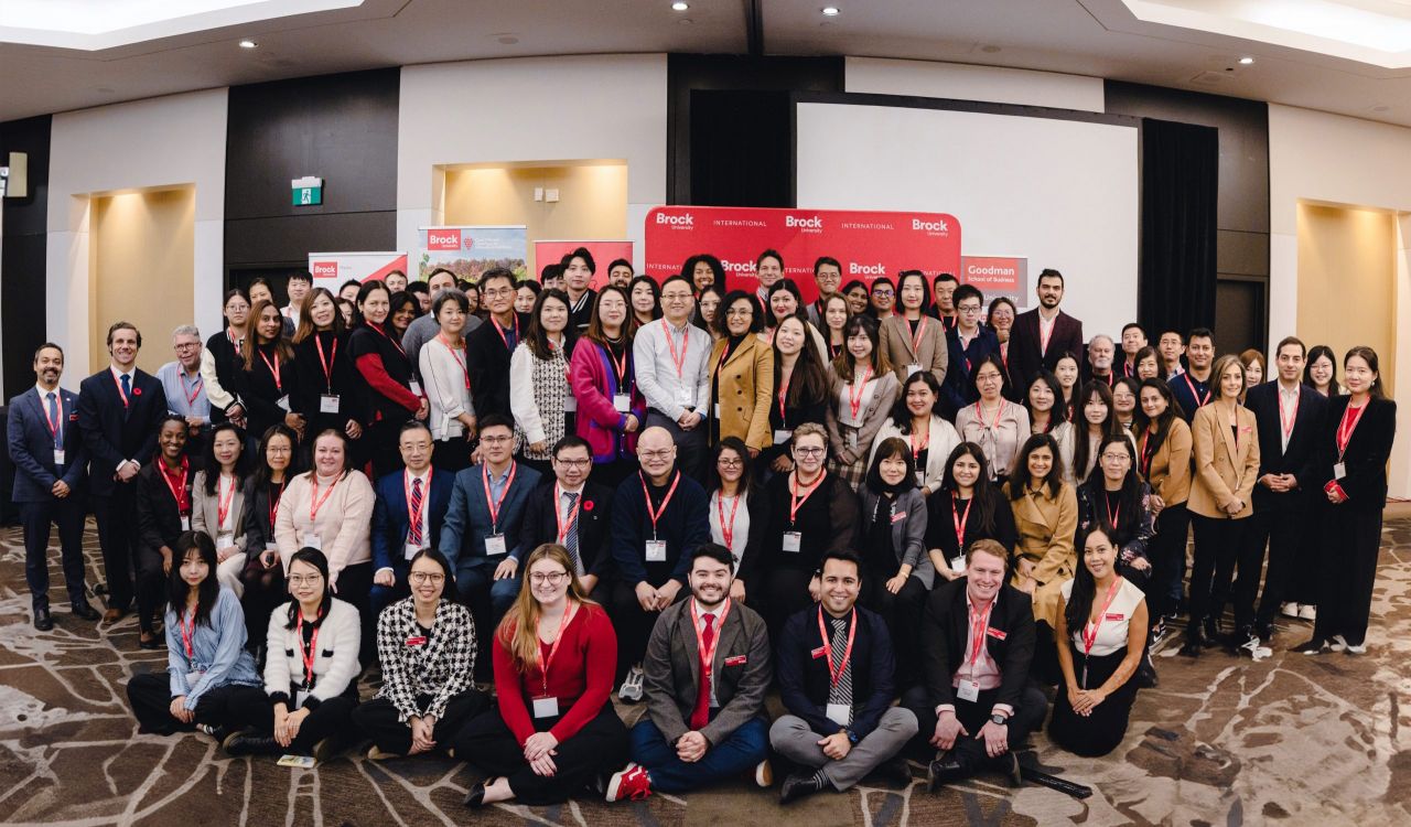 A large group of international education partners pictured in front of a stage in a hotel ballroom.