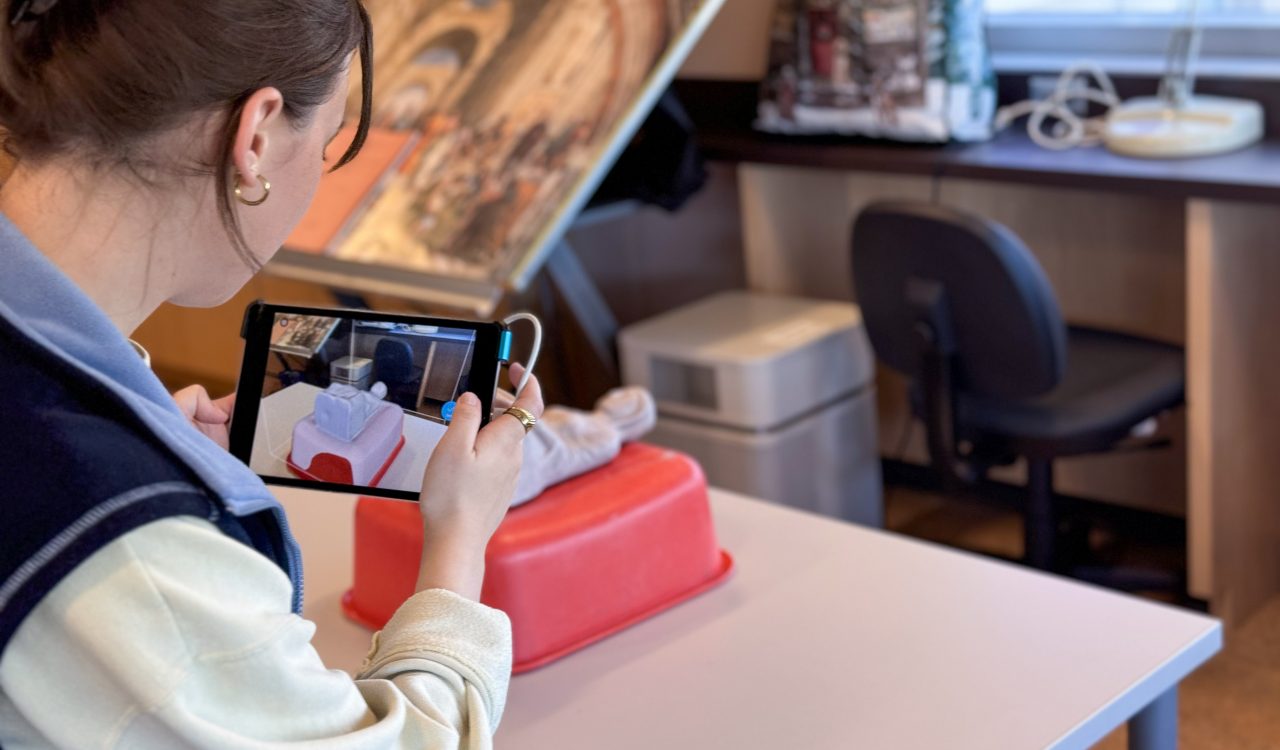 A woman holds an iPad while scanning a small, ancient sculpture in the form of a human bust.