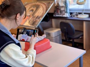 A woman holds an iPad while scanning a small, ancient sculpture in the form of a human bust.