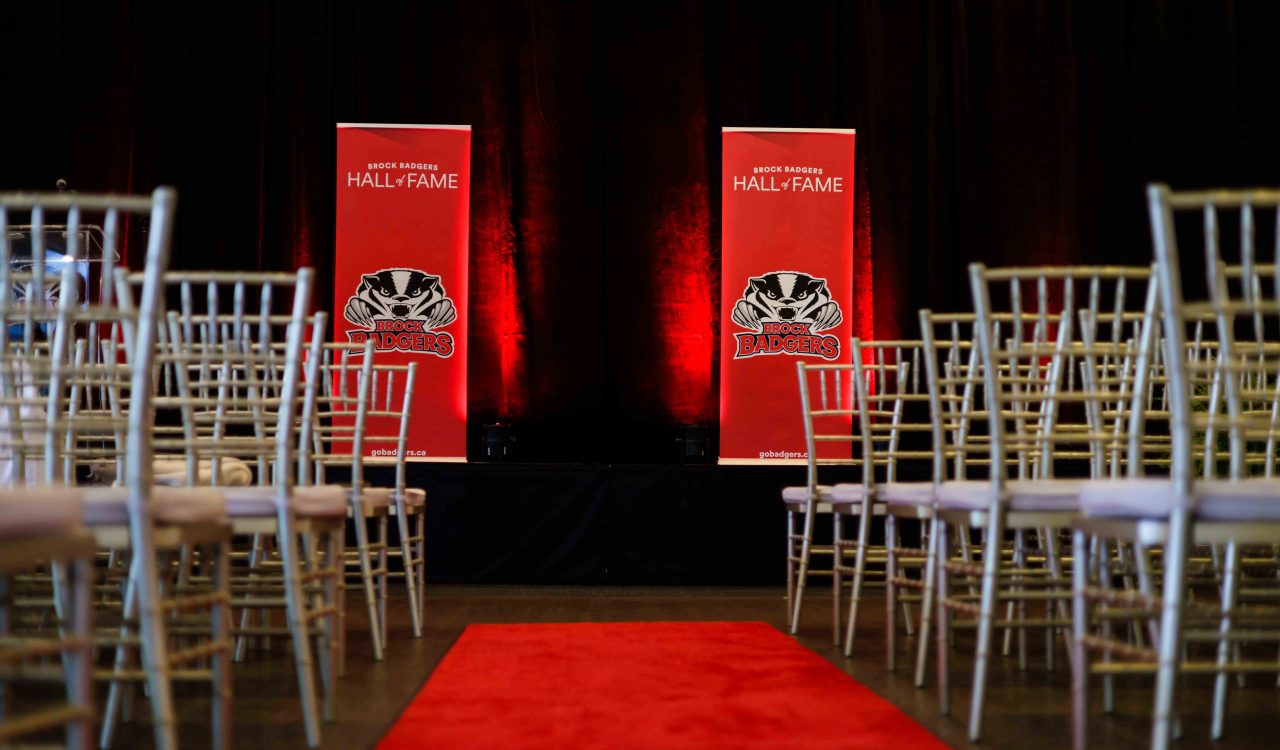 Empty chairs face two Brock Badgers Hall of Fame banners standing at the front of a room.