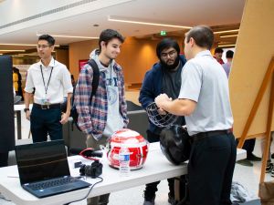 A university student shows a caged helmet to two individuals at a business class presentation.