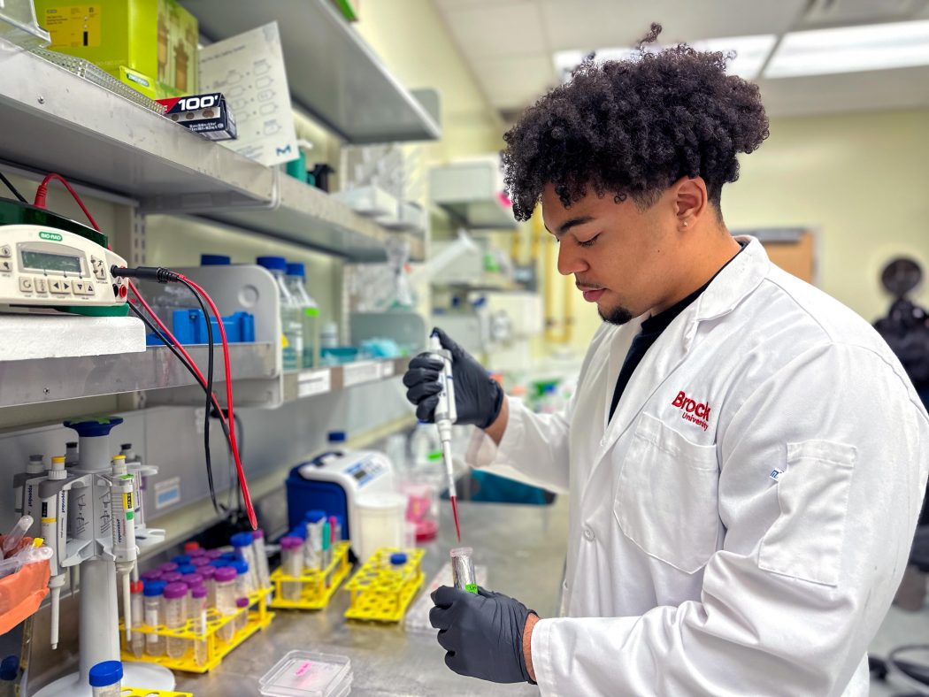 Brock master’s student Jones Nwaeze uses a pipette in Newman Sze’s lab.]