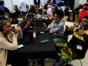 A group of four high school boys and girls smile and give thumbs up while sitting a table inside Brock University.