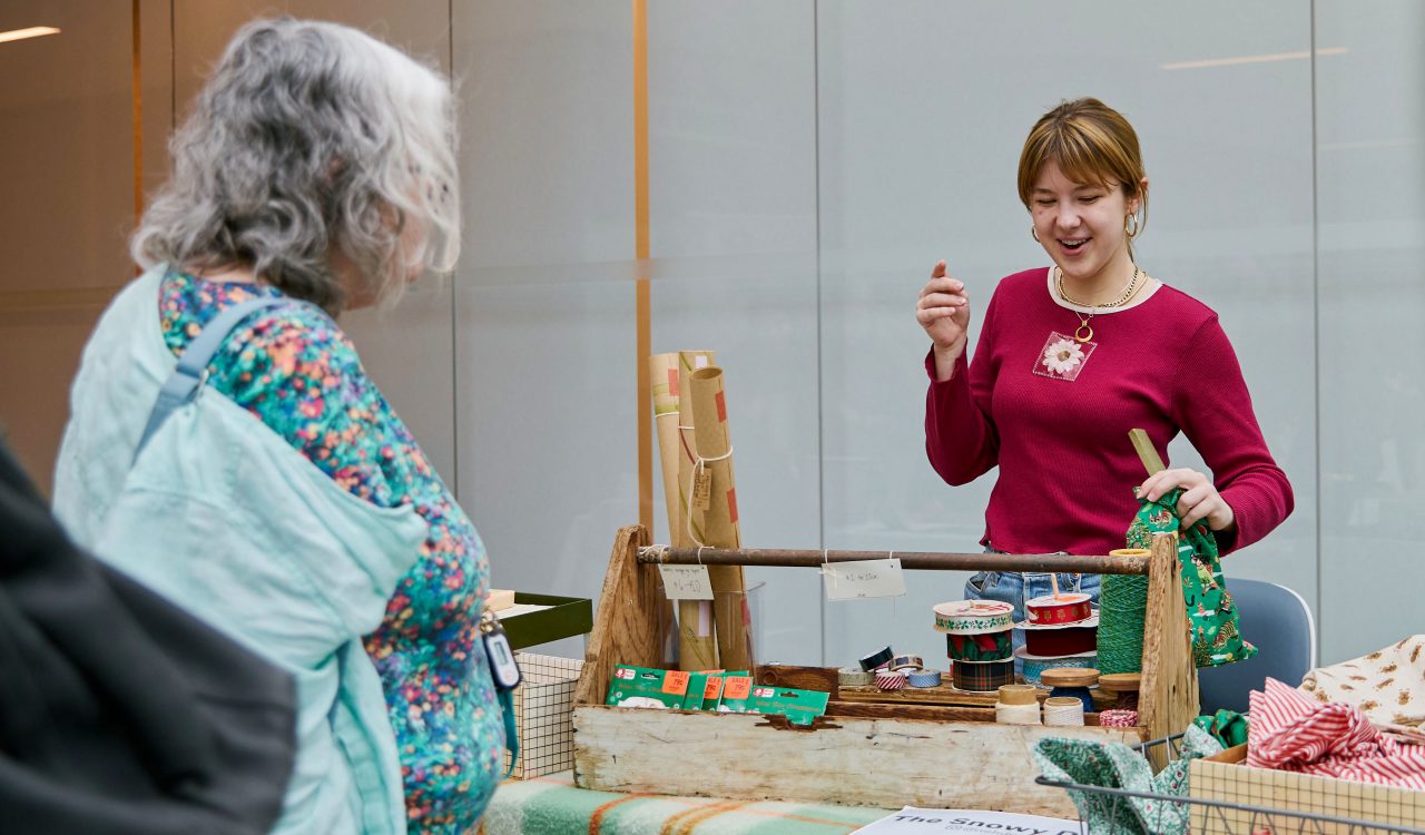 A woman helps a customer at a craft fair.