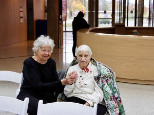 Two women sit together at a public Remembrance Day ceremony.