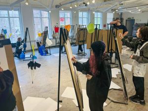 A group of students stand in a circle all at easels drawing in concentration.