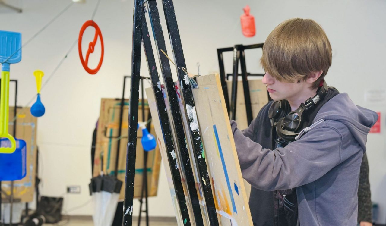 A person stands in an art studio drawing with a pencil at an easel.