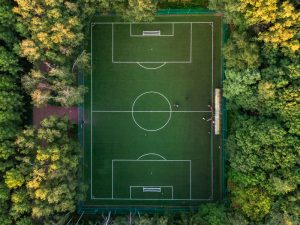 Aerial shot taken with a drone of an outdoor soccer pitch surrounded by trees with a few players on the field.