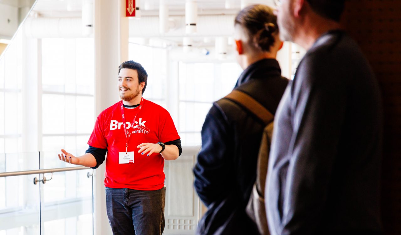 A person in a Brock University t-shirt leads a campus tour.